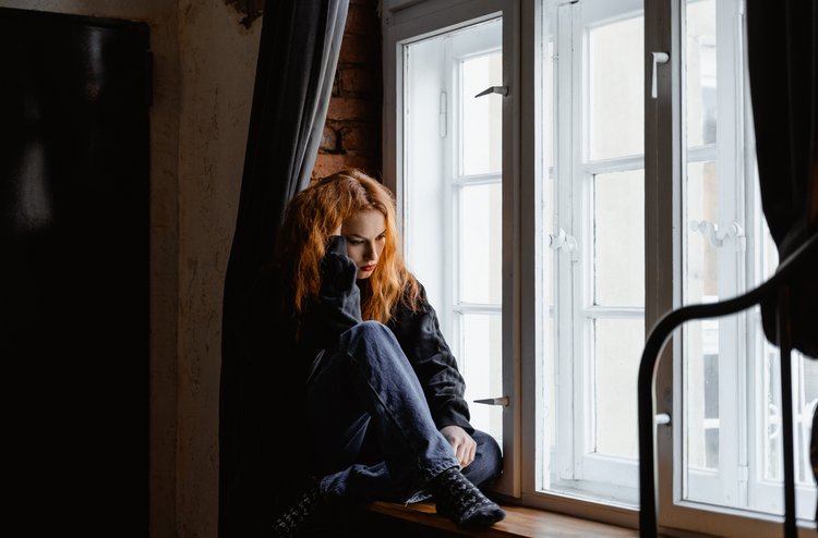 Frau sitzt bekümmert am Fenster