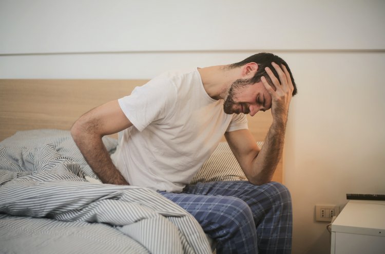 Mann sitzt mit schmerzendem Rücken auf dem Bett