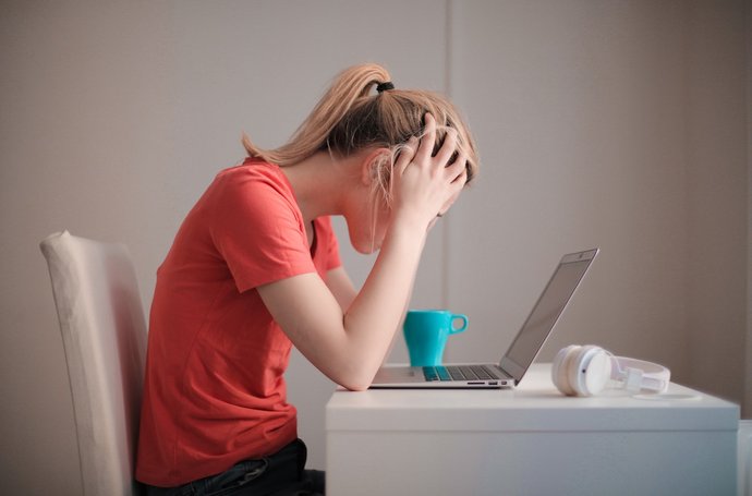Frau blickt auf Laptop, schlägt Hände über dem Kopf zusammen