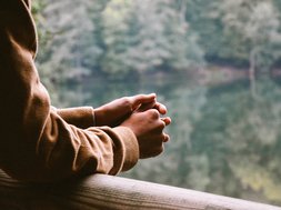 Burnout - Person, die sich an einem Geländer anlehnt mit einem See im Hintergrund 