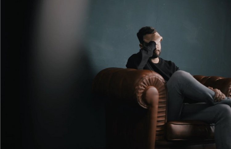 Bipolare Störung - Ein Mann sitzt auf einer Couch mit der Hand vor dem Gesicht