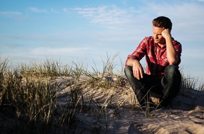Foto eines Mannes mit rot kariertem Hemd, sitzt auf Sanddüne 