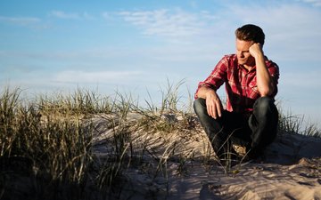 Foto eines Mannes mit rot kariertem Hemd, sitzt auf Sanddüne 