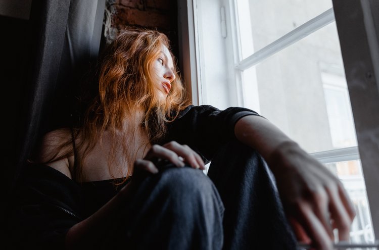 Frau schaut in Gedanken aus Fenster