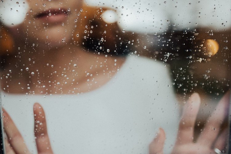 Artikel Midlife-Crisis Frau am Fenster mit Regentropfen